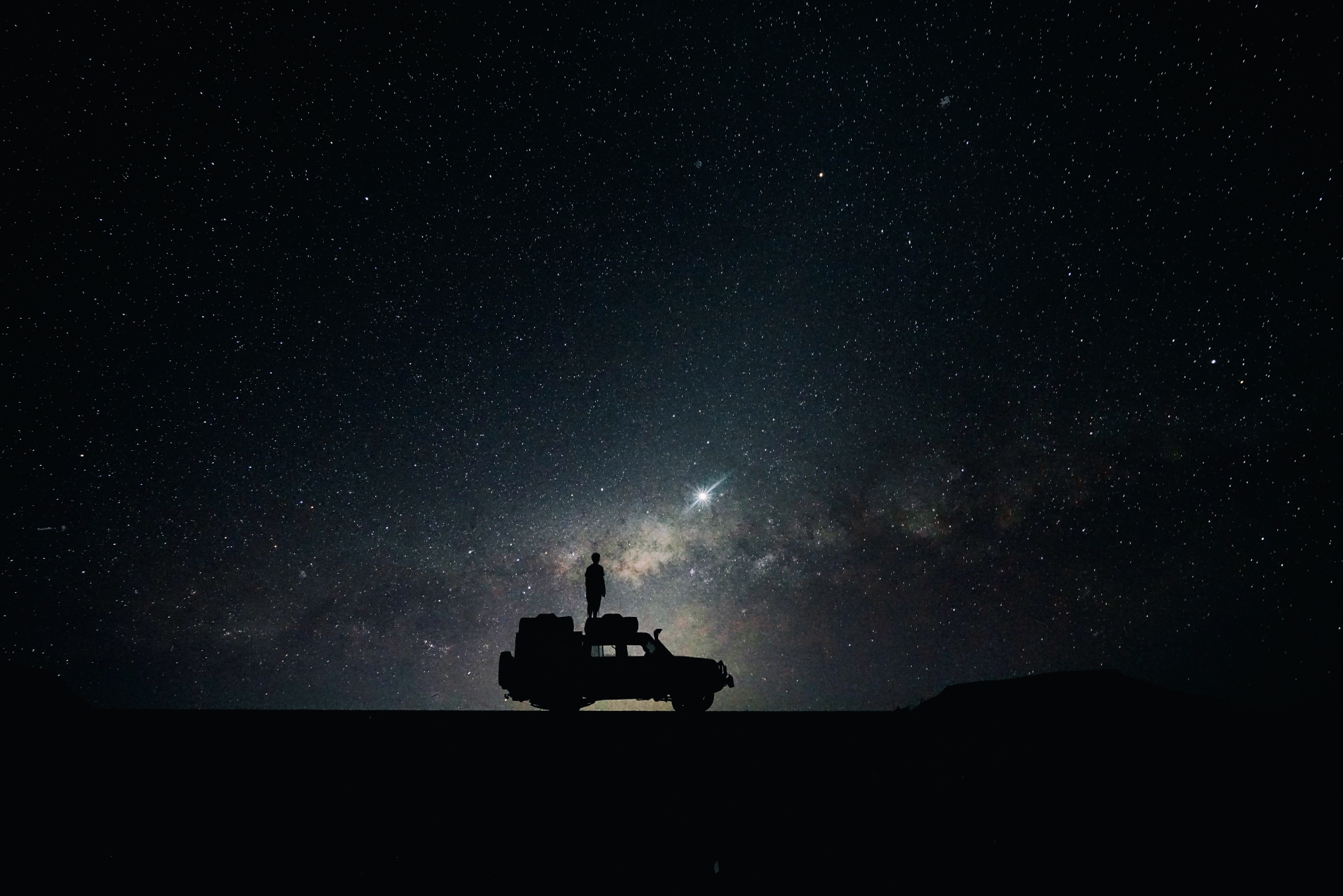 man steht auf einem jeep in der wüste bei nacht und betrachtet den sternenhimmel afrikas auf einer exklusiven rundreise und safari